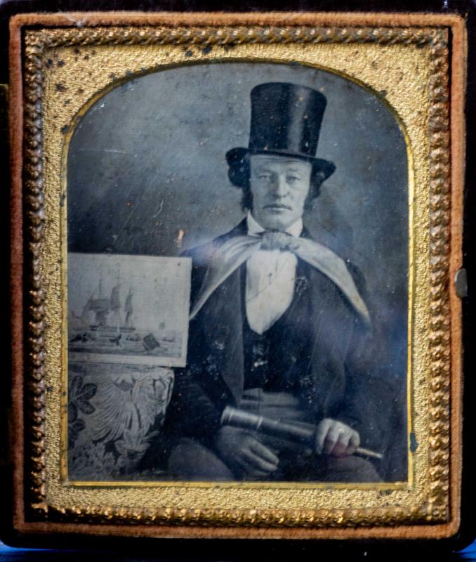 Seated Whale Man wearing top hat and holding in his hand a telescope and on the table next to him is a "Whaling Print by Huggins", American, circa 1850.